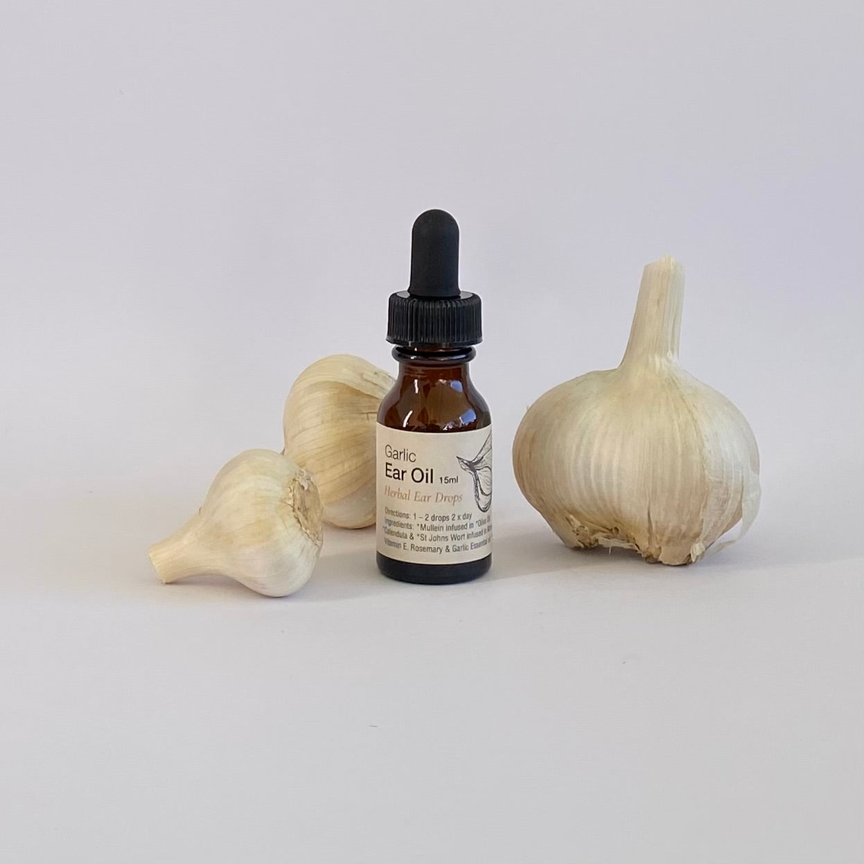Bottle of Garlic Ear Oil with garlic bulbs on a white background