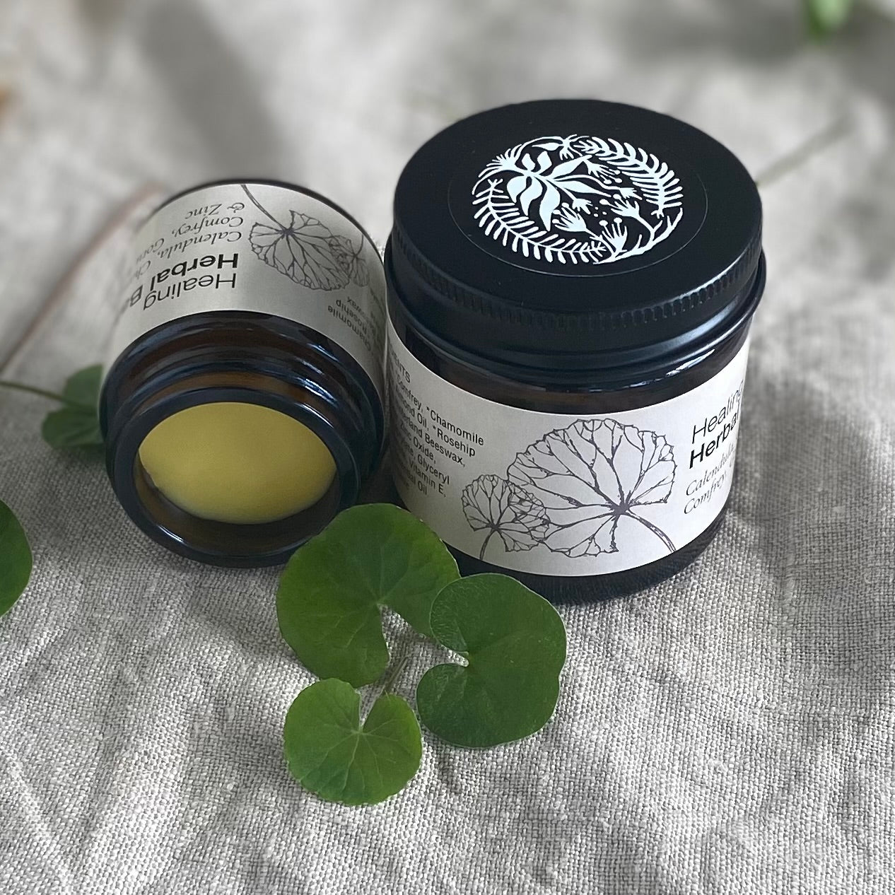 two jars of Healing Herbal balm on a linen background with gotu kola