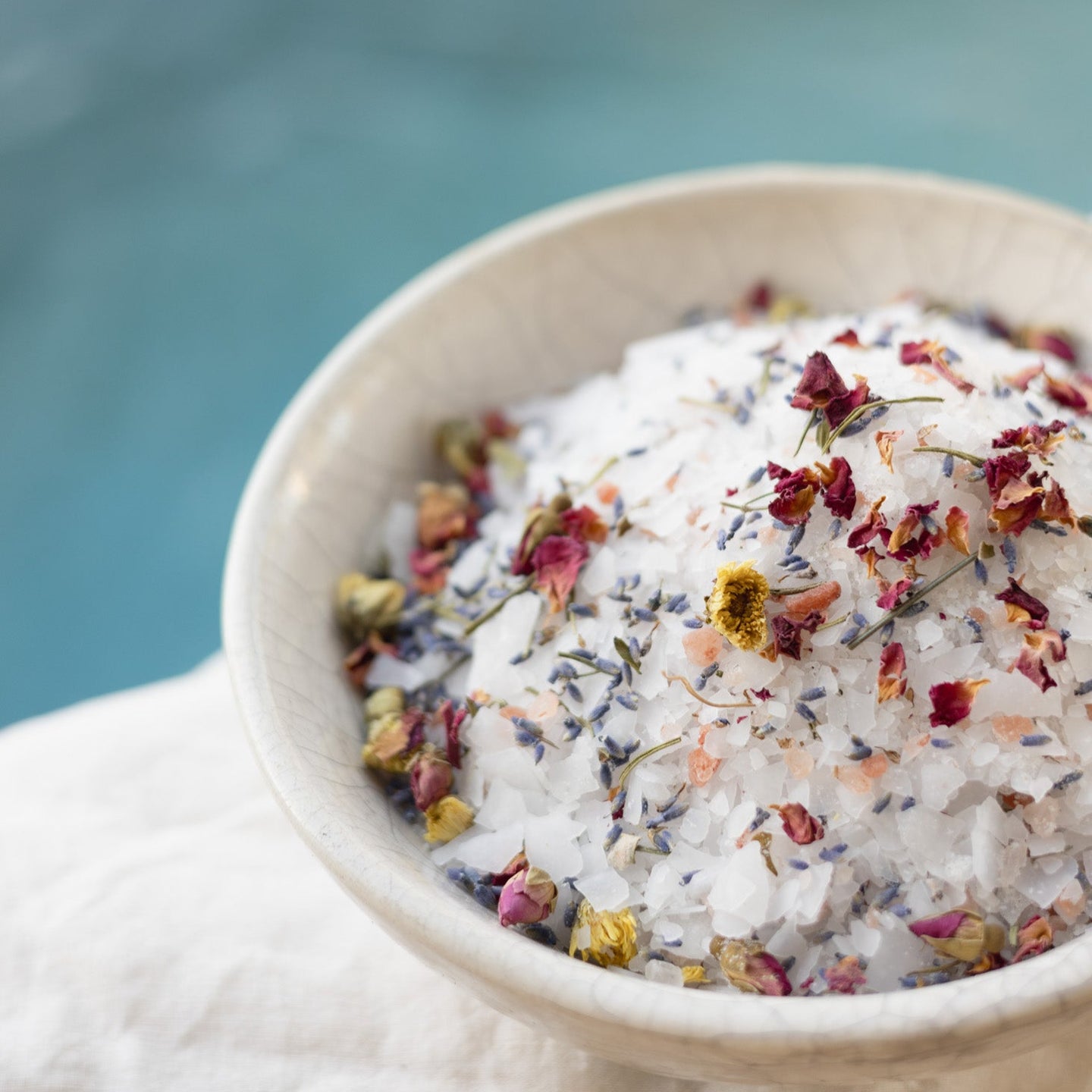 Bowl of bath salts with flowers and petals on a blurred natural background