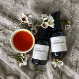 two bottles of organic rosehip oil with a bowl of rosehip oil on a linen background with flowers