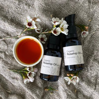 two bottles of organic rosehip oil with a bowl of rosehip oil on a linen background with flowers